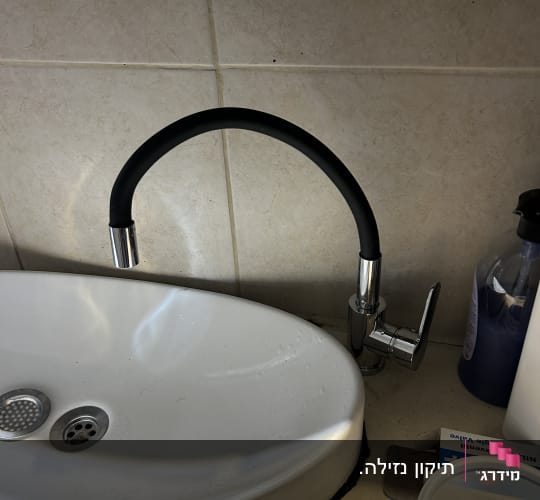 ברז שחור וכיור לבן על רקע קיר אריחים